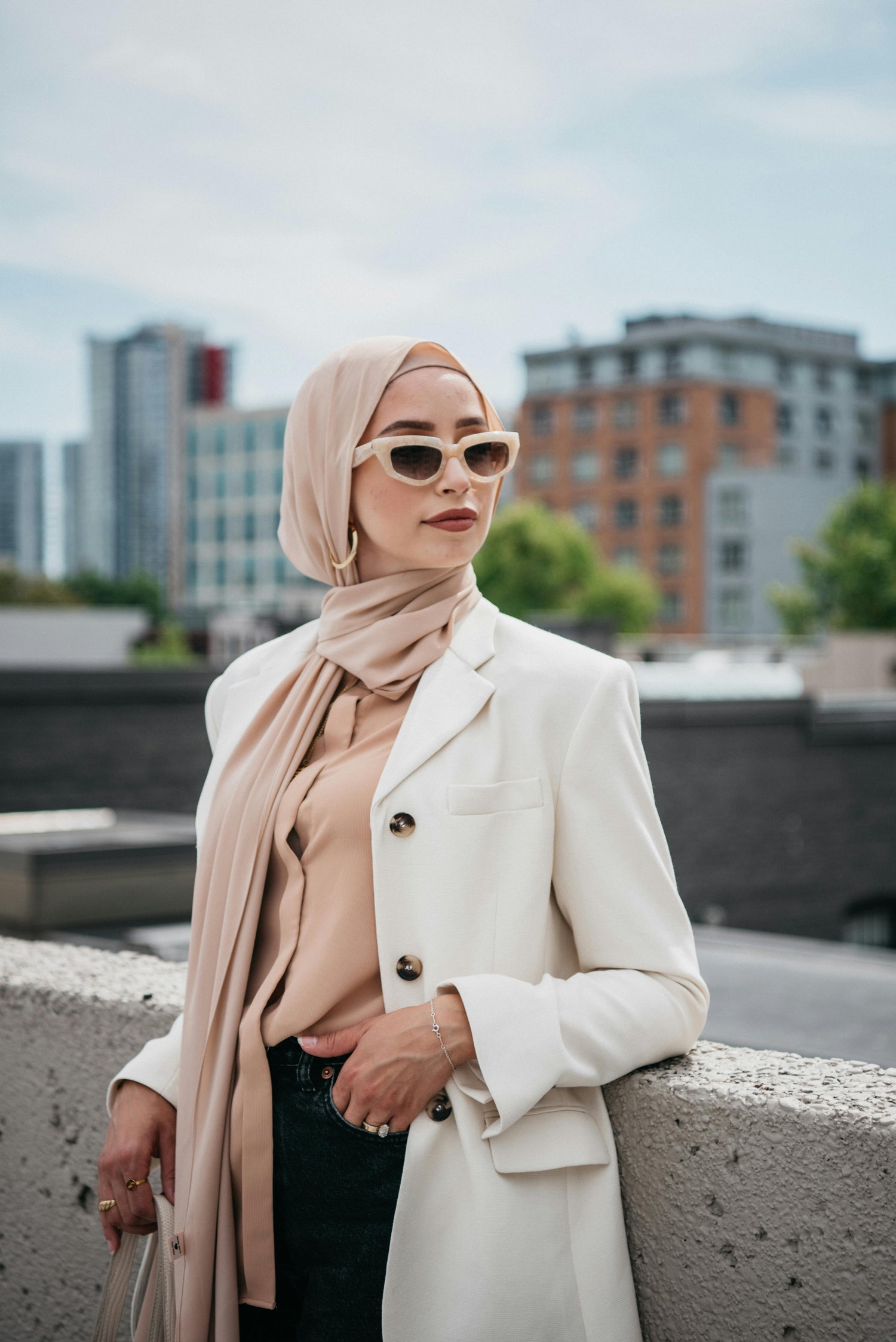 Woman wearing beige chiffon hijab with blazer in modern city setting, stylish modest fashion outfit with elegant lightweight hijab