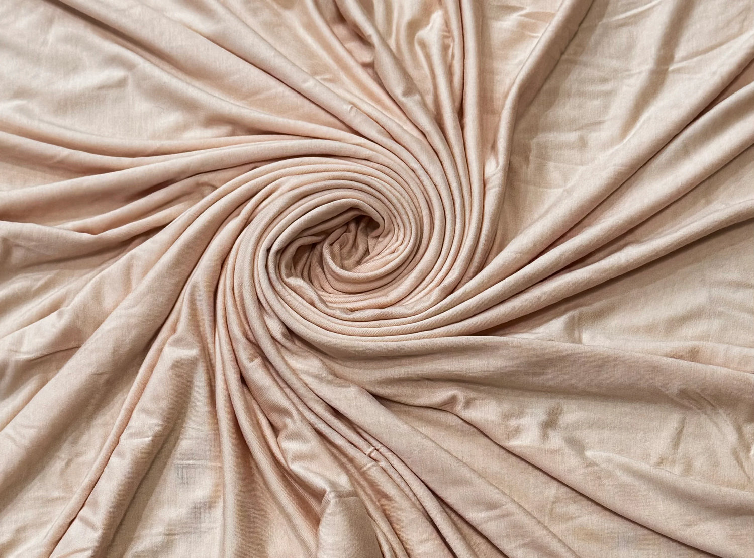 Close-up of soft neutral jersey hijab fabric arranged in smooth folds, showing texture and drape.