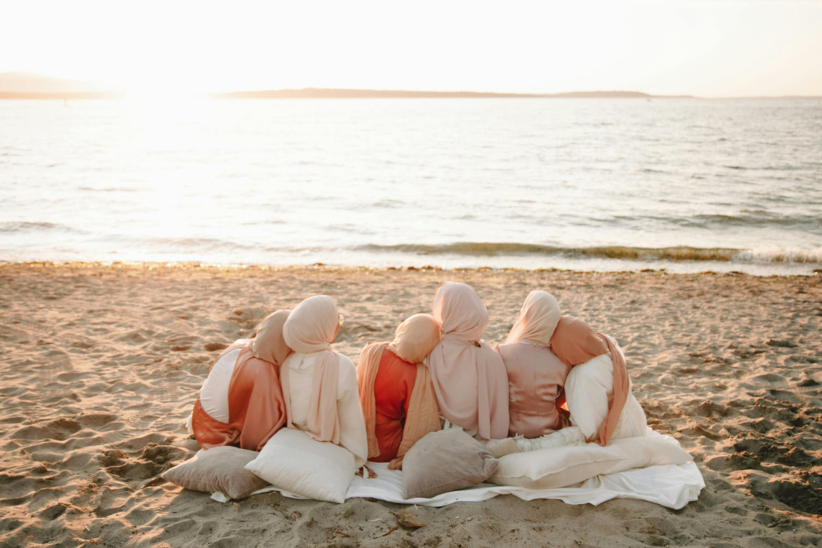 Group of women in hijab sitting together by the sea at sunset, representing a calm and supportive start to the hijab journey