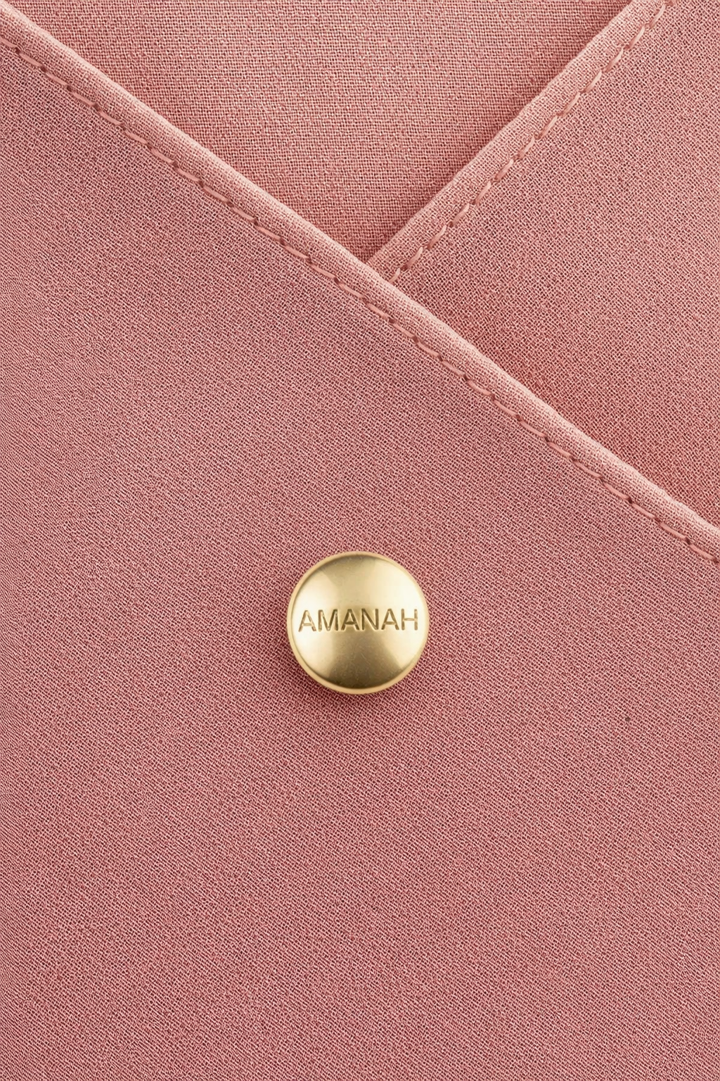 Close-up of a gold hijab magnet engraved with “AMANAH” securing a soft blush hijab fabric.