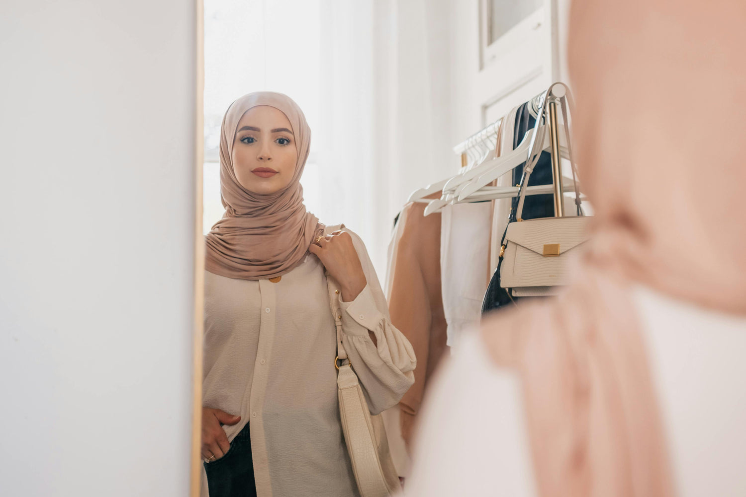Woman wearing taupe hijab styling modest outfit in front of mirror, elegant neutral fashion look with soft chiffon hijab